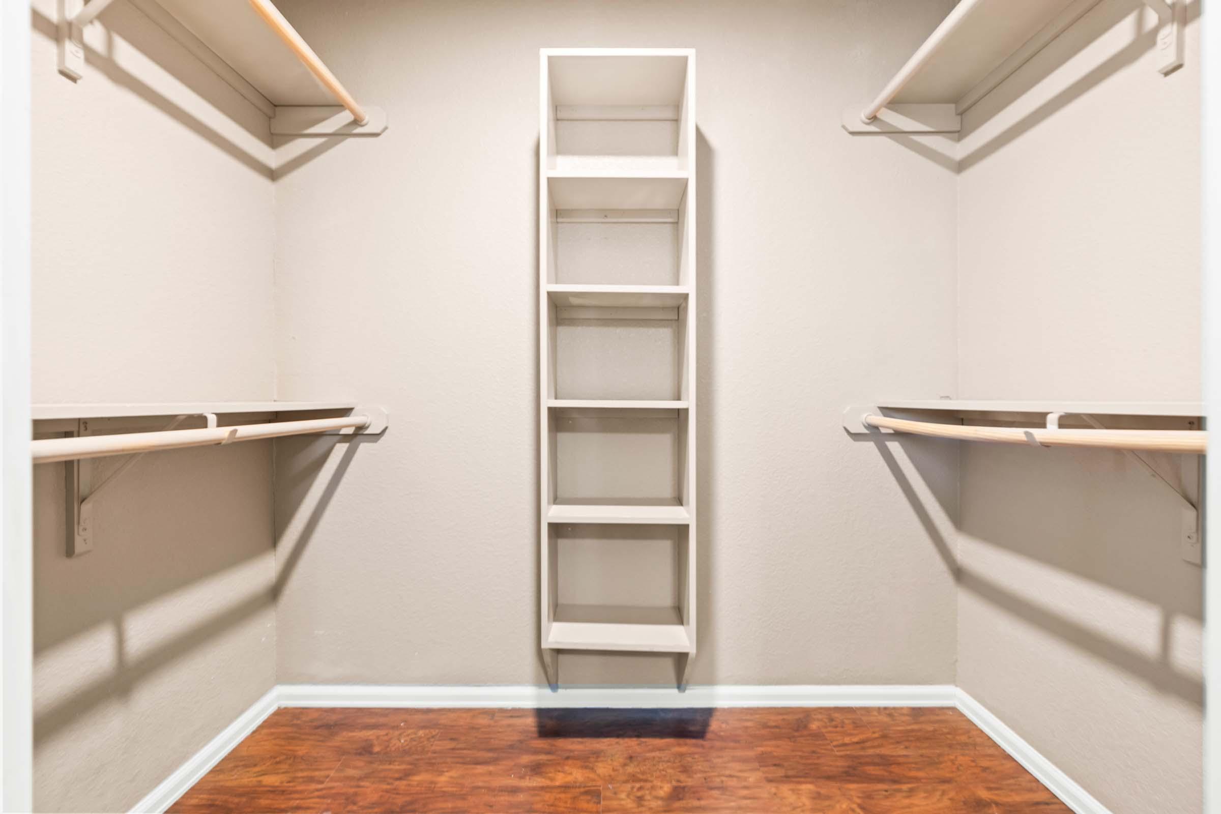 A clean, empty closet with light-colored walls and wooden flooring. It features two horizontal shelving units on either side and a central, tall white shelf unit with five open compartments, providing a minimalist storage solution.