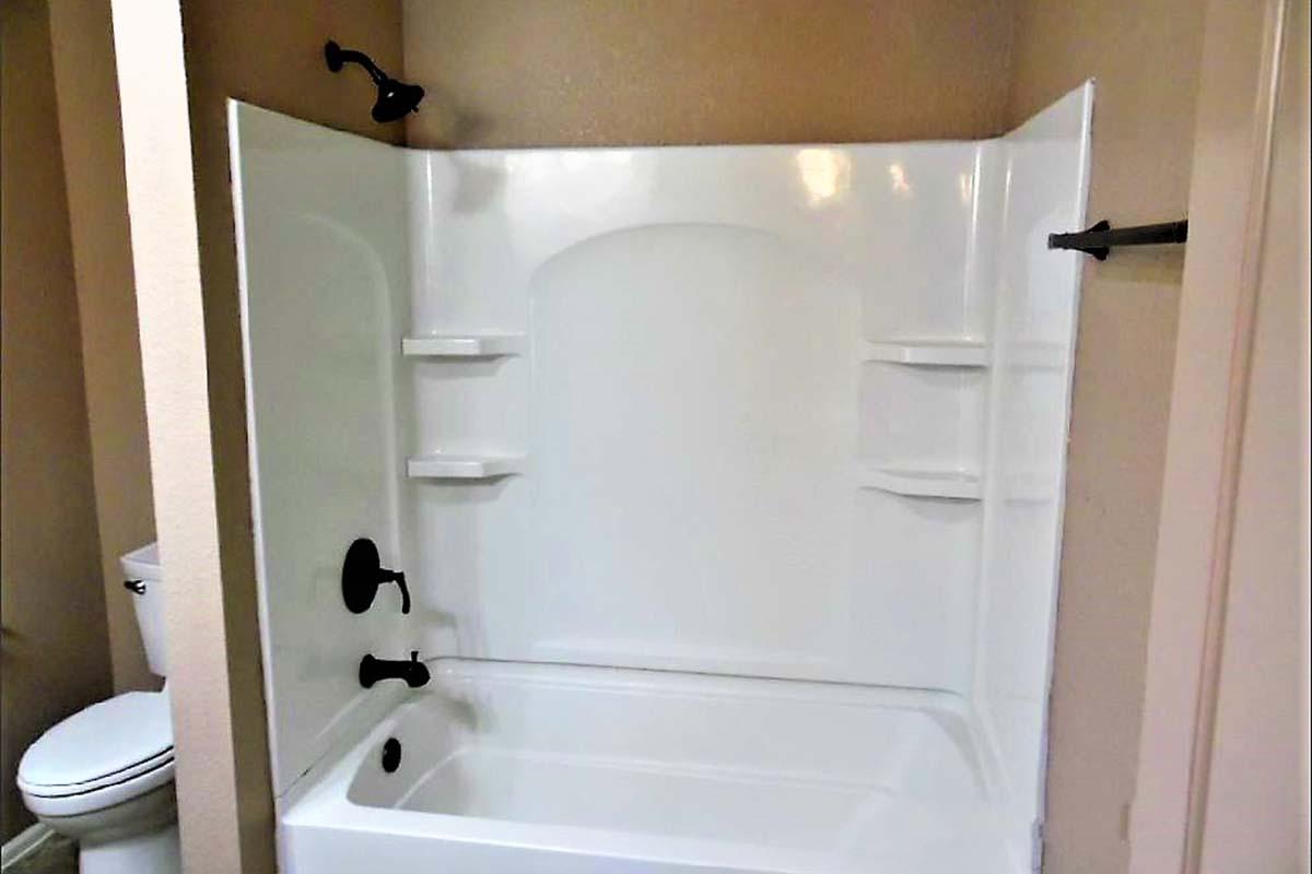 A clean, modern bathroom featuring a white bathtub with black fixtures, designed with built-in shelves on the wall for storage. A toilet is visible in the background, and the walls are painted in a light color, creating a spacious and bright appearance.