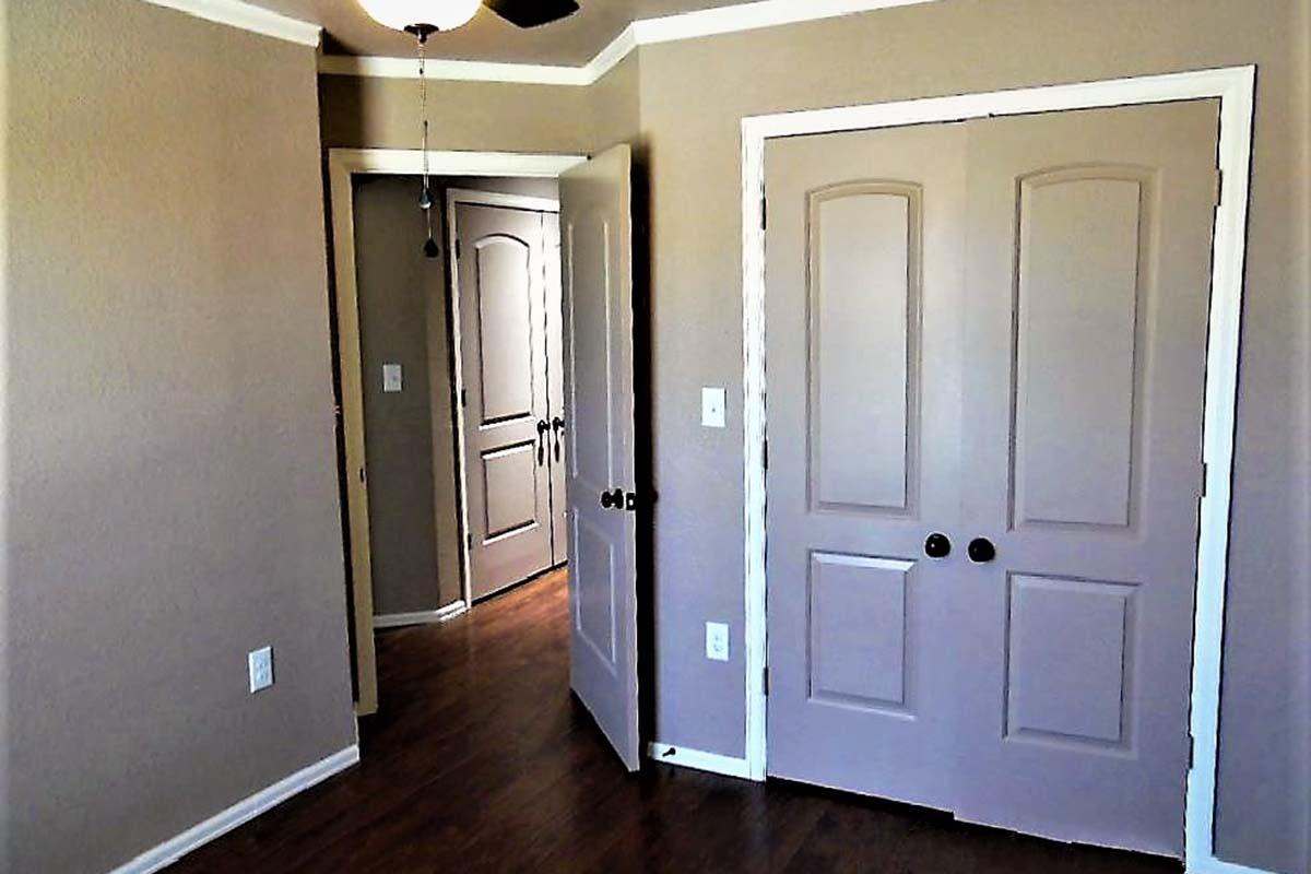 Interior of a room featuring two closed doors and a ceiling fan. The walls are painted in a light brown color, with a light wood floor. One door leads to another area, while the other appears to be a closet. Natural lighting creates a warm atmosphere in the space.