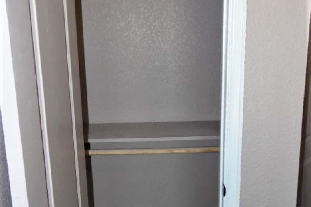 Empty closet or storage space with a single shelf and a clothes rod, featuring plain walls and a door slightly ajar.