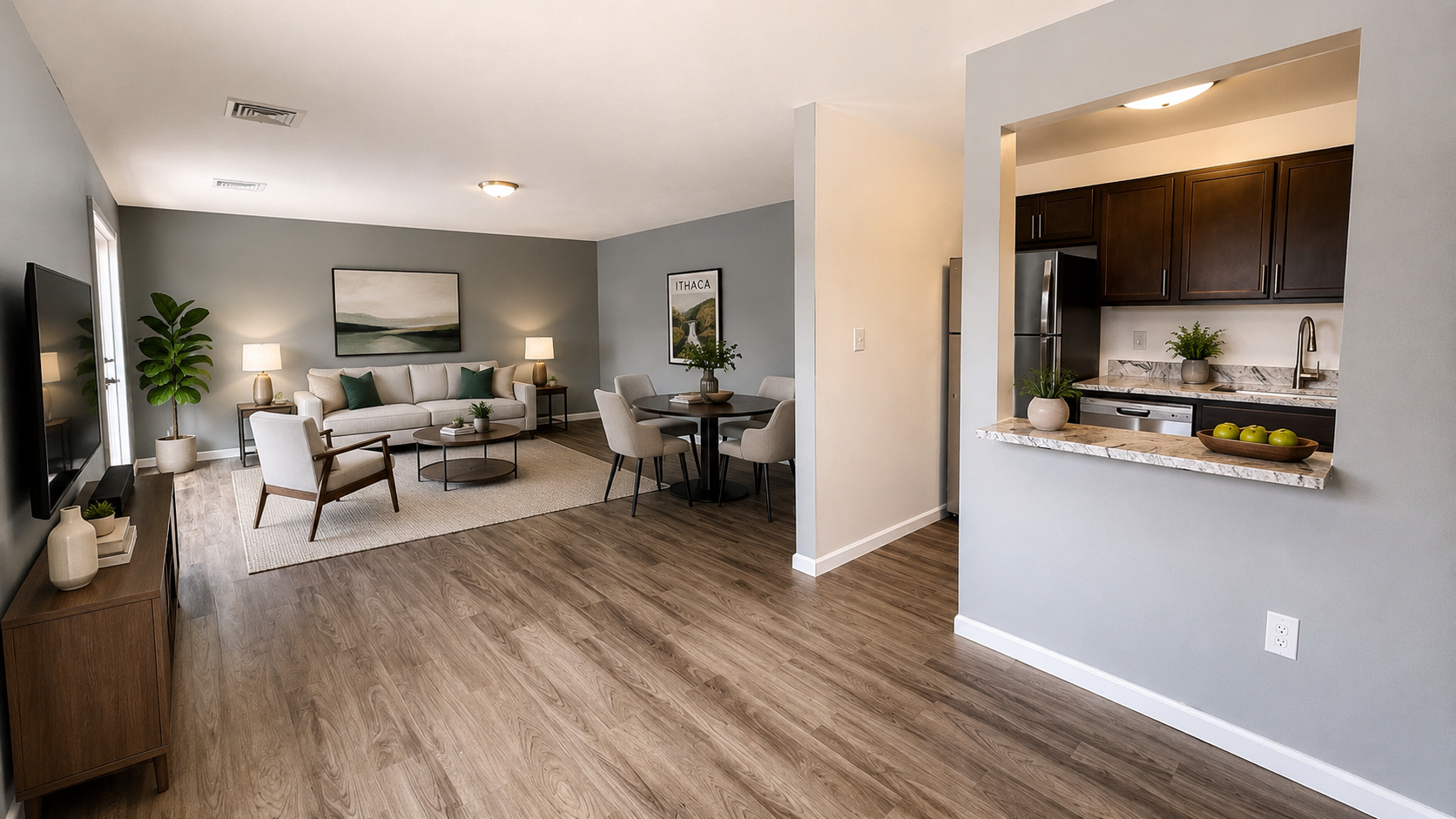 A modern living space featuring a cozy seating area with a light-colored sofa and armchairs, a round dining table, and a kitchenette with dark cabinets. The walls are painted in soft gray, and there are decorative plants and art pieces that add warmth to the room. The flooring is light wood.