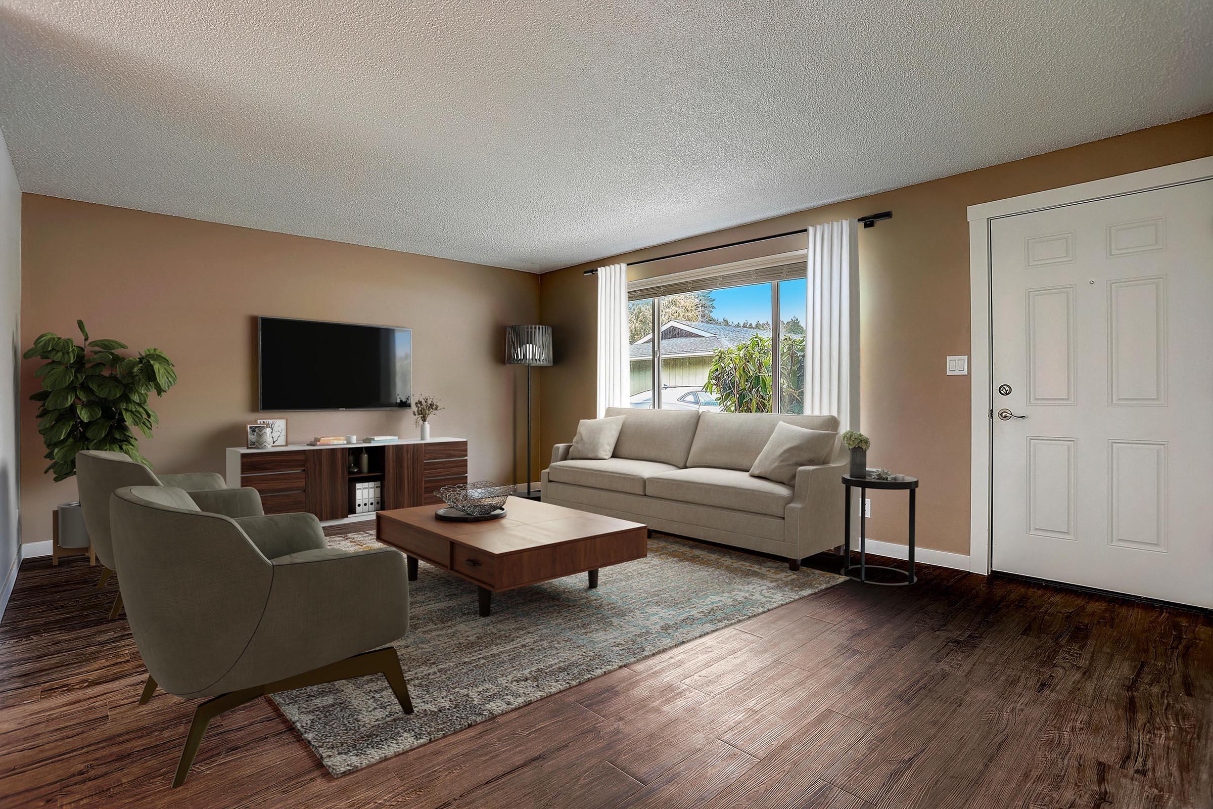 A cozy living room featuring a beige sofa, two green chairs, a wooden coffee table, and a TV mounted on a cabinet. Natural light enters through the window, illuminating the space. A potted plant adds a touch of greenery, and the front door is visible on the right.