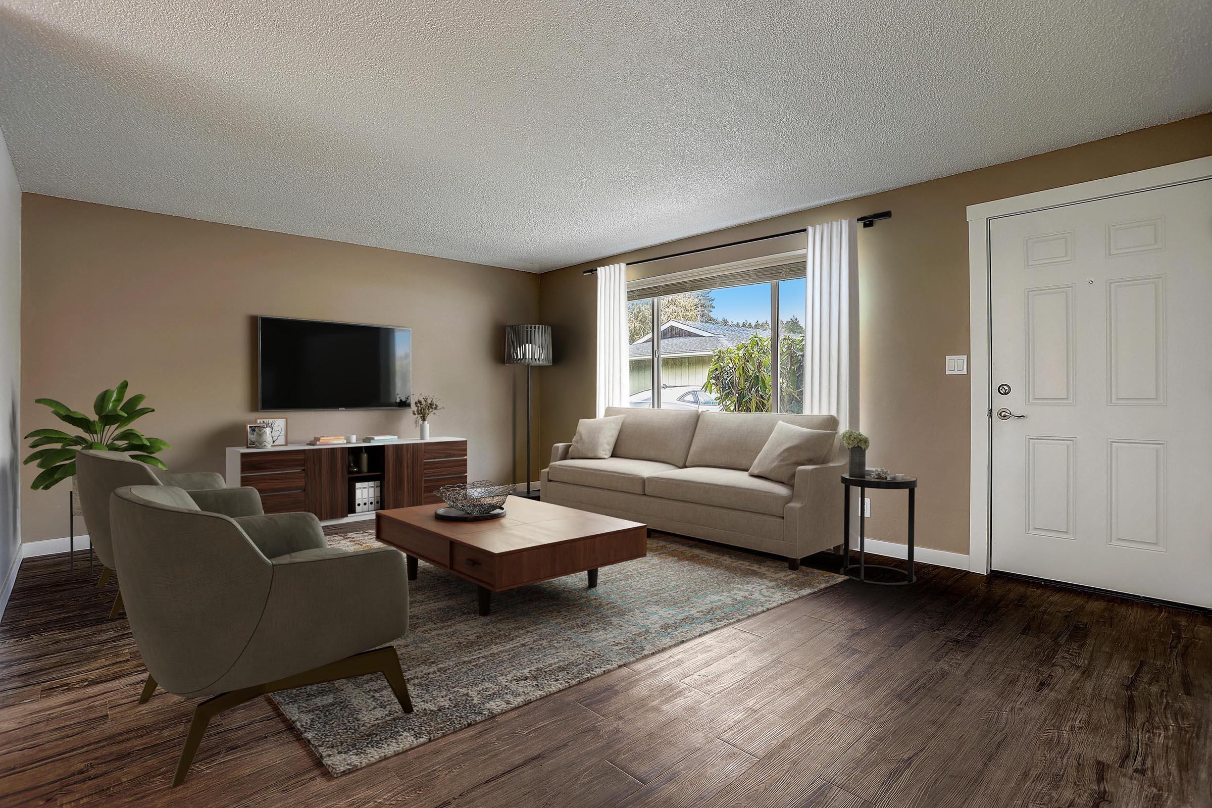 A cozy living room featuring a light-colored sofa, two armchairs, a wooden coffee table, and a television unit. Natural light streams in through windows, illuminating a plant in the corner and creating a warm, inviting atmosphere. The door to the outside is visible, adding to the openness of the space.