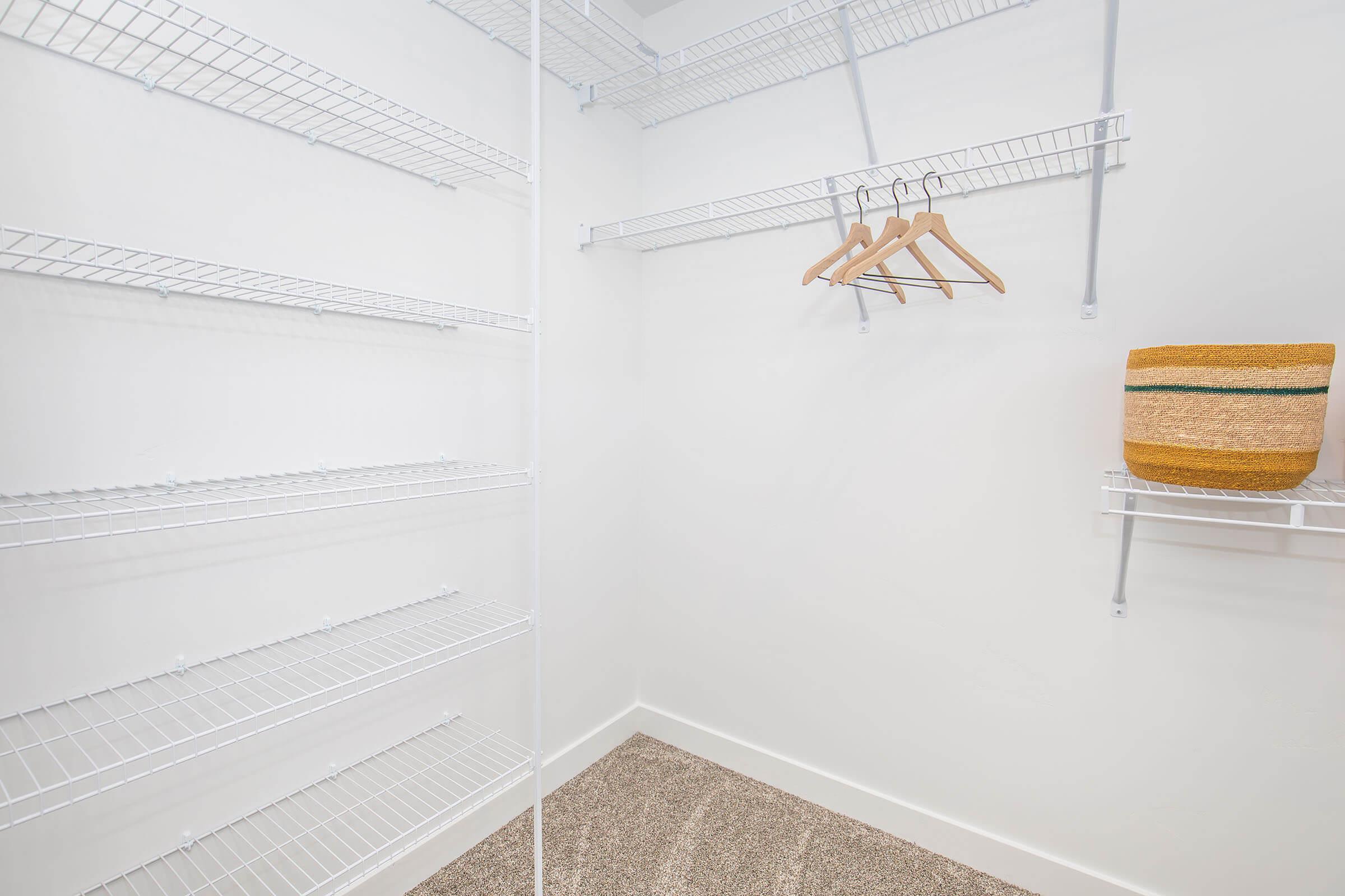 A tidy, empty closet featuring white wire shelving and a few wooden hangers hanging on a rod. A woven basket sits on a shelf to the right. The walls and flooring are light in color, creating a bright and spacious atmosphere.