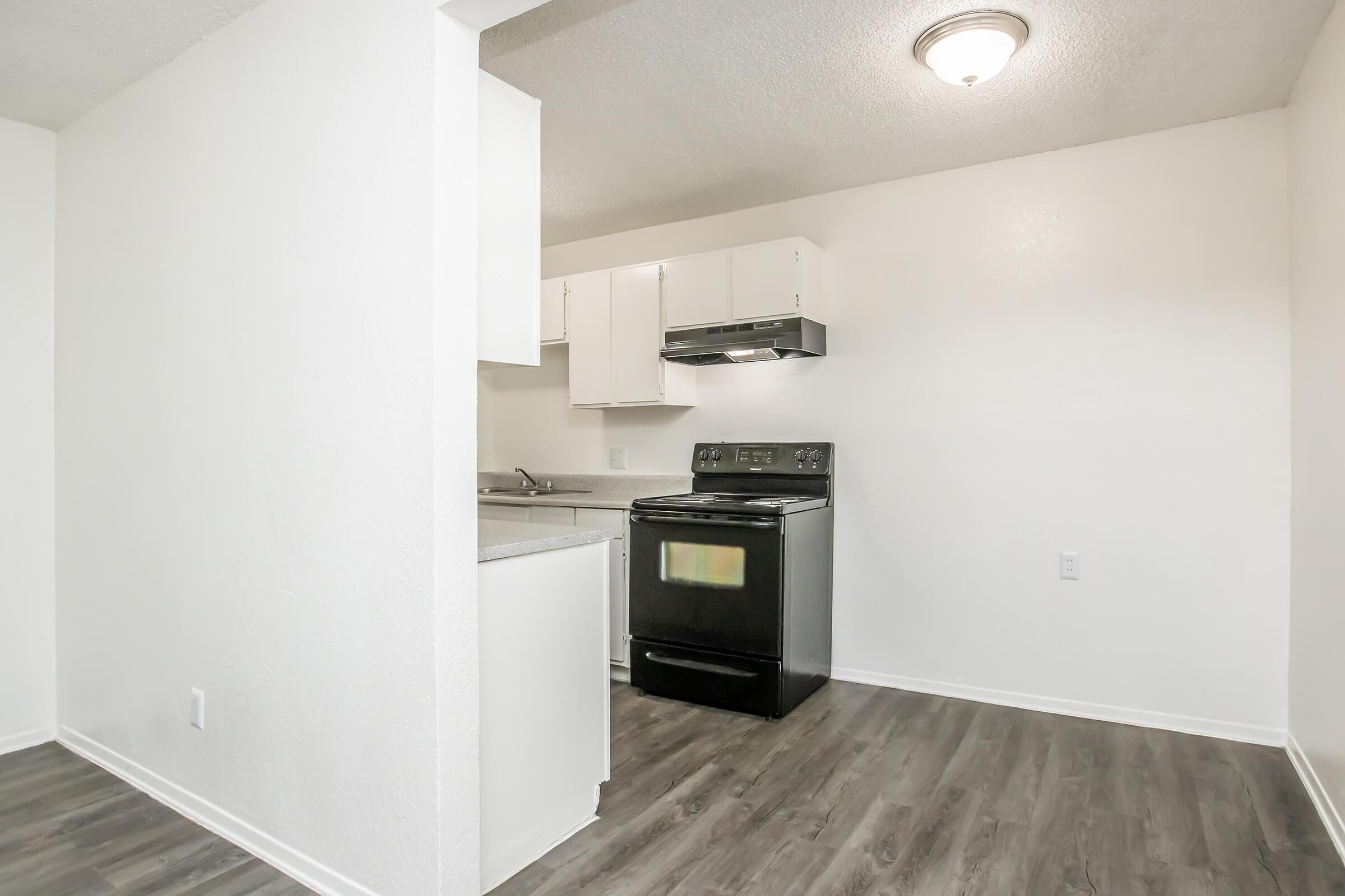 Modern kitchen with white cabinets and a black oven. The space features a light-colored wall, laminate flooring, and a ceiling light fixture. There is a countertop area adjacent to the stove, designed for convenience and functionality in a compact layout.