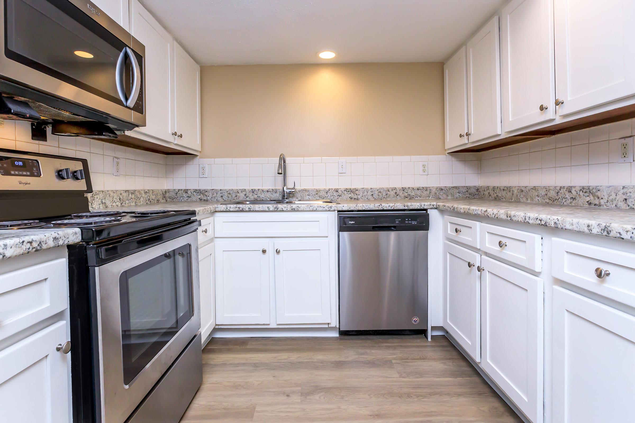 Modern kitchen with white cabinetry, granite countertops, stainless steel appliances, including an oven, microwave, and dishwasher. The space features a neutral wall color and warm lighting, creating a bright and inviting atmosphere.