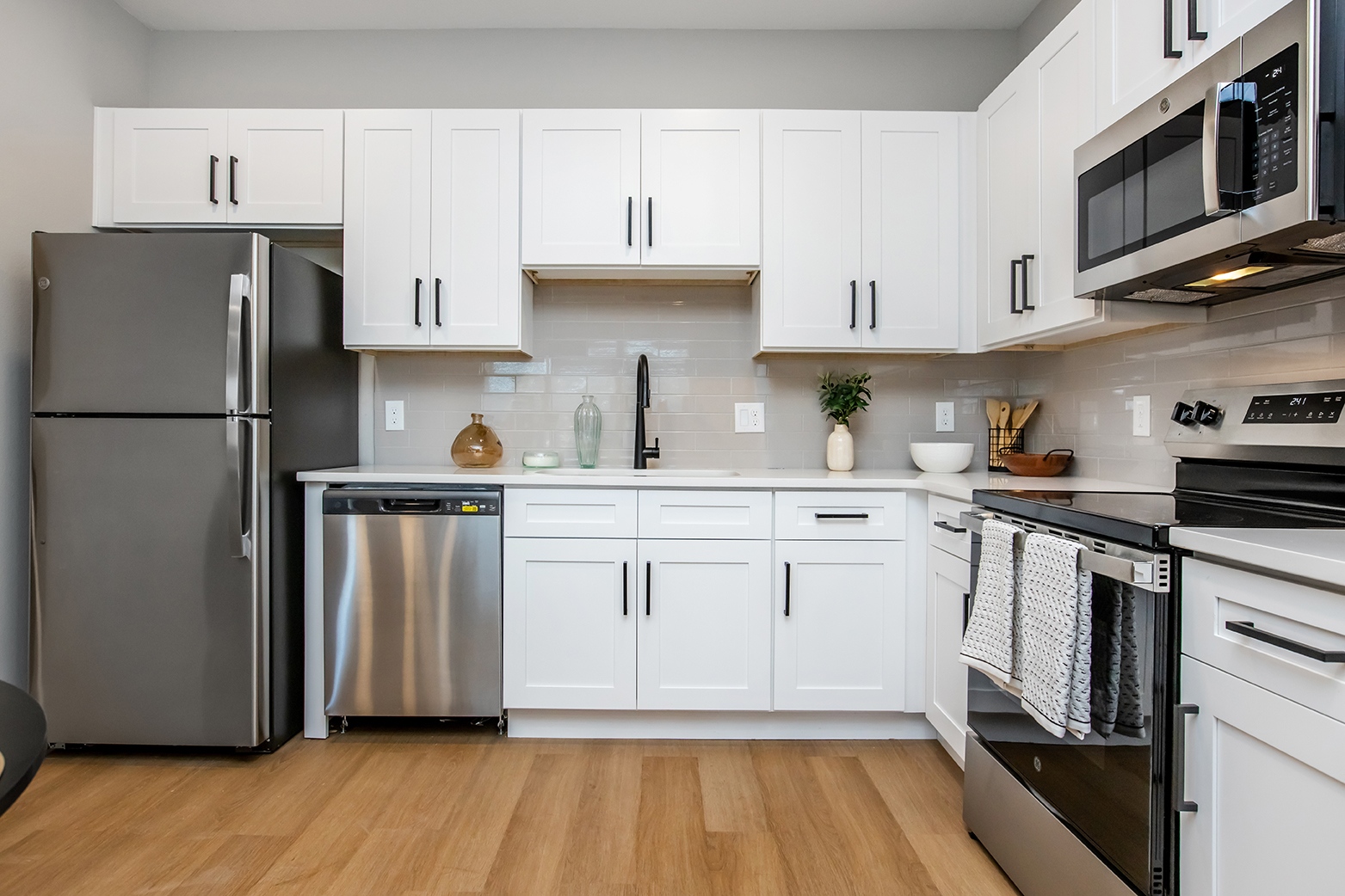 Modern kitchen featuring white cabinetry, stainless steel appliances including a refrigerator, dishwasher, and oven, and a sleek countertop. A minimalist aesthetic with wooden flooring, decorative items on display, and an overall clean, contemporary design.