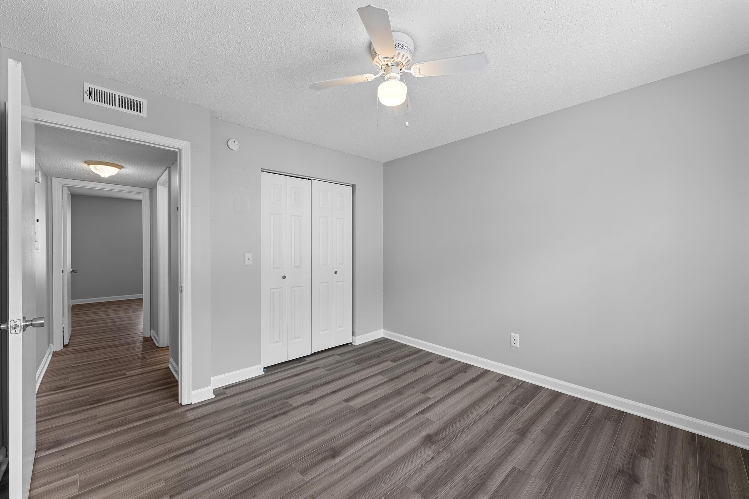 A spacious room featuring light gray walls, a ceiling fan, and hardwood floors. There are two closed closet doors on one wall, and doorways leading to other areas of the home. The overall atmosphere is bright and inviting, with ample natural light.