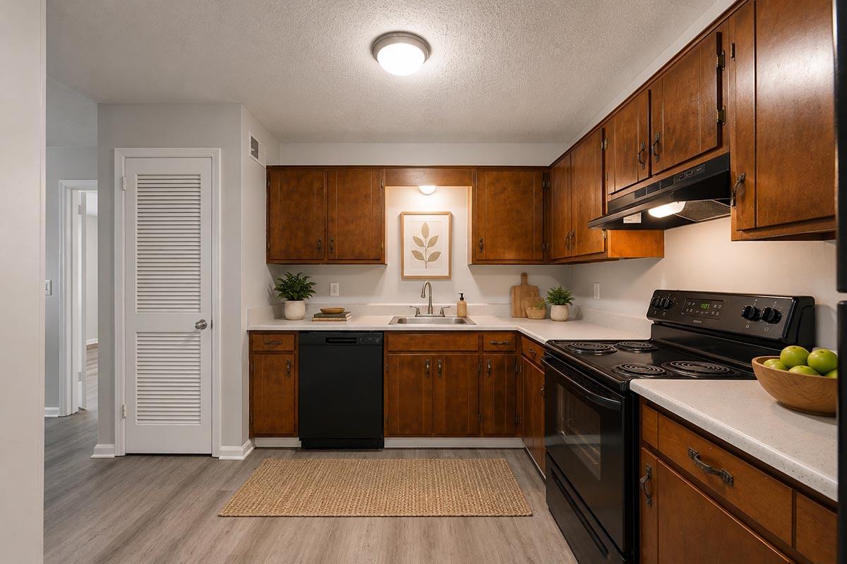 Modern kitchen featuring wooden cabinetry, a black dishwasher, and two black ovens. It has a white countertop with a sink, decorative plants, and a framed botanical print on the wall. A jute rug is placed on the floor, and a bowl of green apples is on the counter, creating a warm and inviting atmosphere.