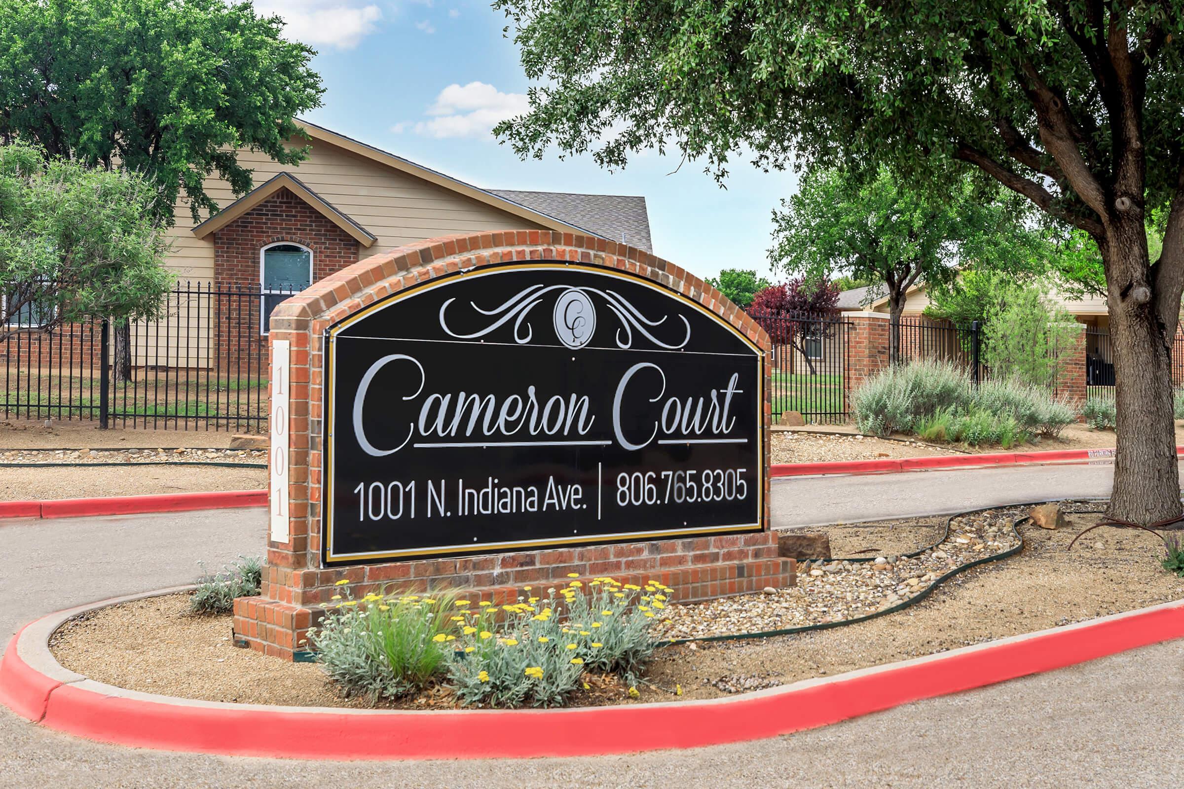 Sign for Cameron Court, located at 1001 N. Indiana Ave. Includes a phone number, 806-765-8305. The sign features a decorative design and is surrounded by landscaping with trees and shrubs, set against a clear blue sky.