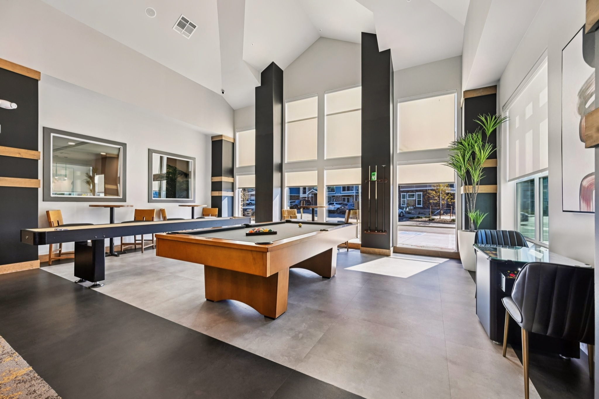 A modern recreational room featuring a billiard table, sleek furniture, and large windows allowing natural light. The space has a stylish design with neutral colors and a touch of greenery from a potted plant, creating a welcoming atmosphere for relaxation and socializing.