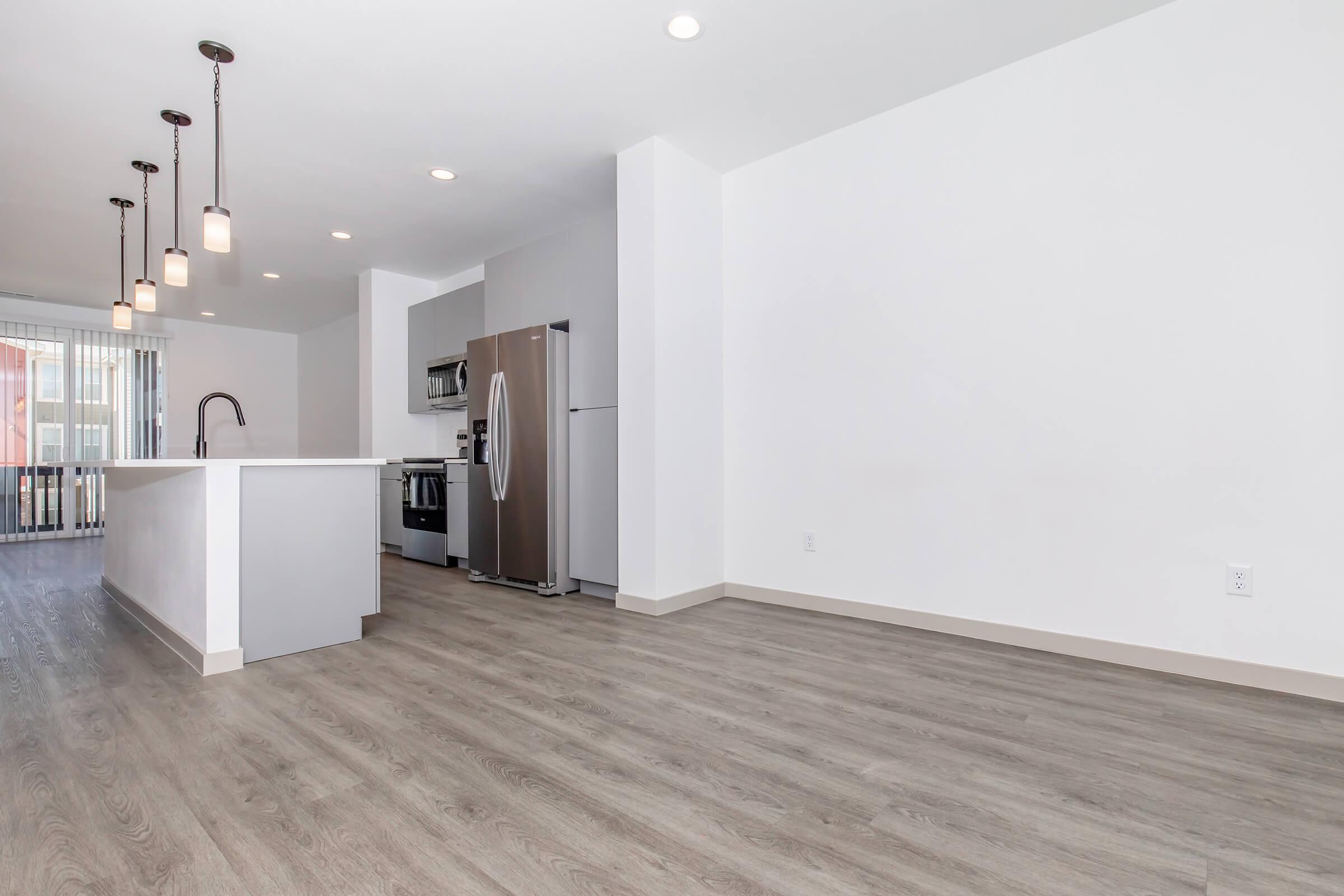Modern kitchen and dining area featuring a spacious layout with light wood flooring. The kitchen includes stainless steel appliances, a large island with seating, and pendant lighting. Large windows provide natural light, enhancing the open atmosphere of the room.