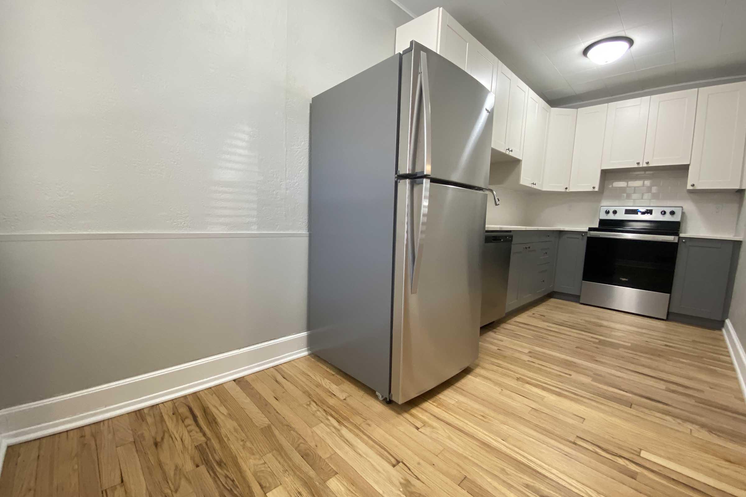 Modern kitchen featuring stainless steel appliances, including a refrigerator and oven, with light-colored cabinets and wooden flooring. The space has a clean and inviting layout with ample natural light.