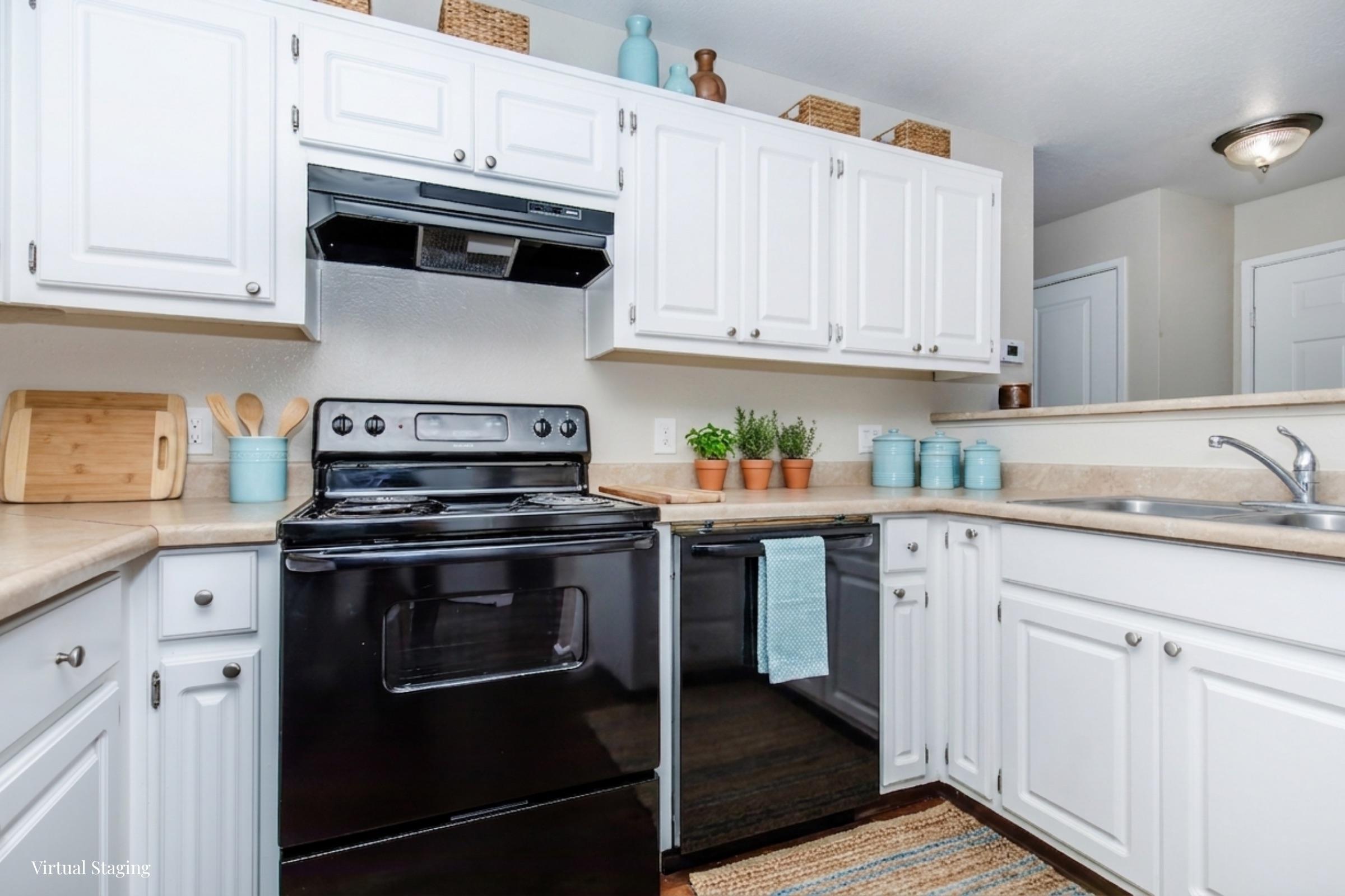 A well-organized kitchen featuring white cabinetry, black appliances, and a neutral countertop. Potted herbs are displayed along with decorative jars on the shelves. A woven rug adds warmth to the space, and the layout includes a stove, sink, and open shelving for easy access to kitchen essentials.