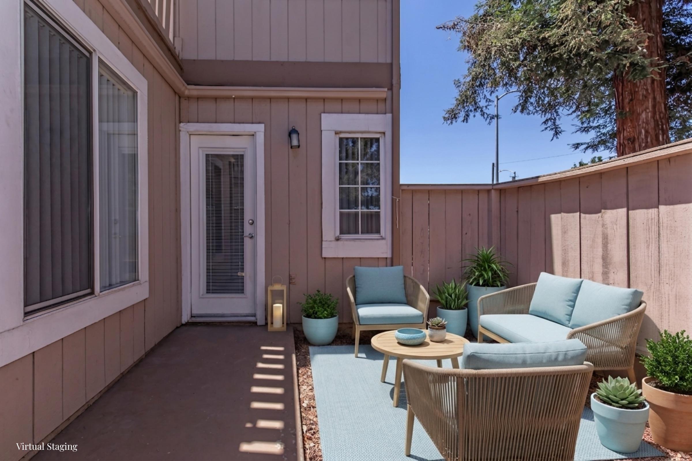 A cozy outdoor patio space featuring light blue seating with cushions, a small round table, and potted plants. The wall is painted in a soft beige, with a door leading inside. Sunlight streams in, creating a bright, inviting atmosphere.