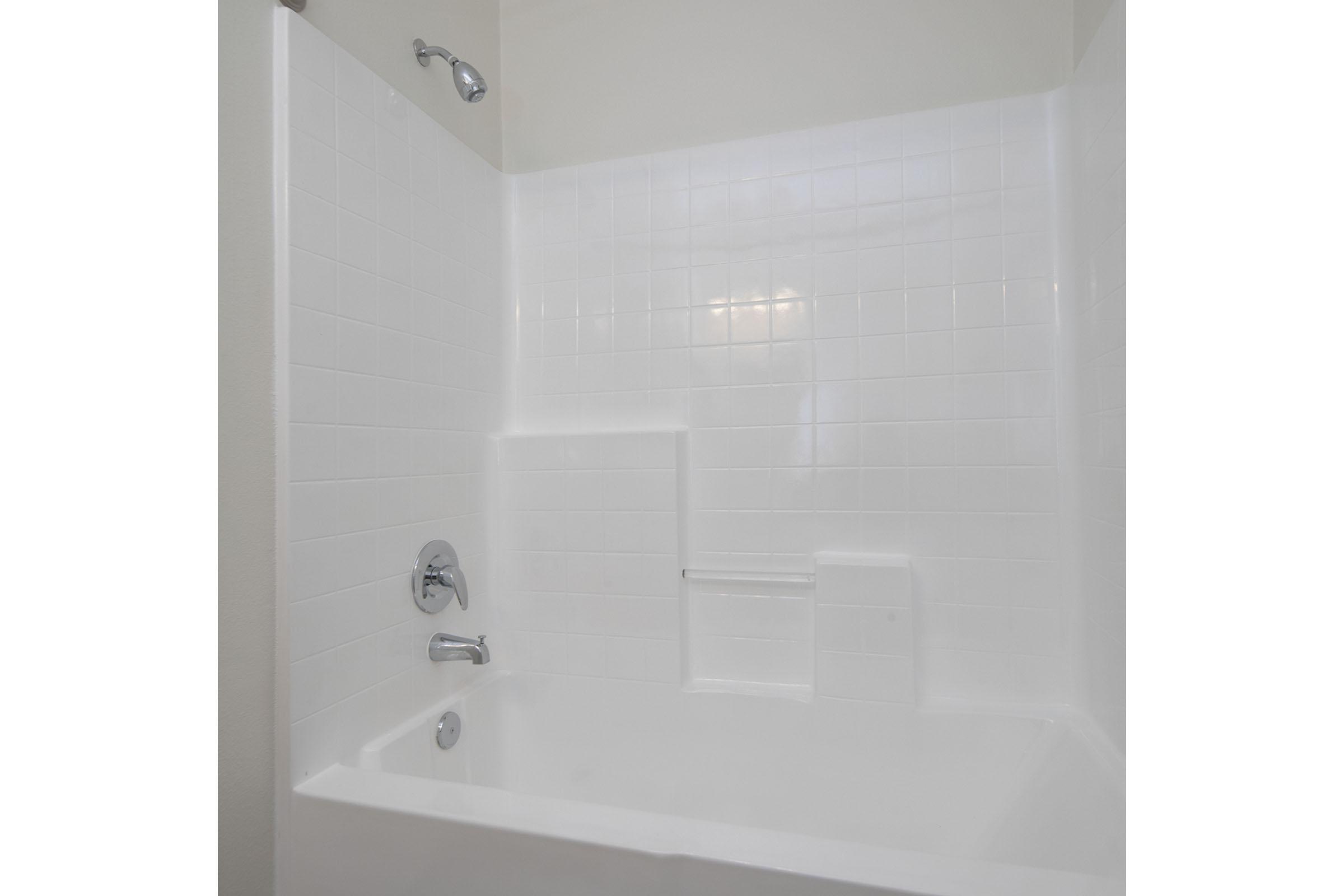 A clean, modern bathroom featuring a white tiled shower and bathtub. The shower has a chrome faucet and a showerhead, with a sleek design that creates a bright and airy atmosphere. The walls are a smooth, light color, enhancing the overall fresh appearance of the space.