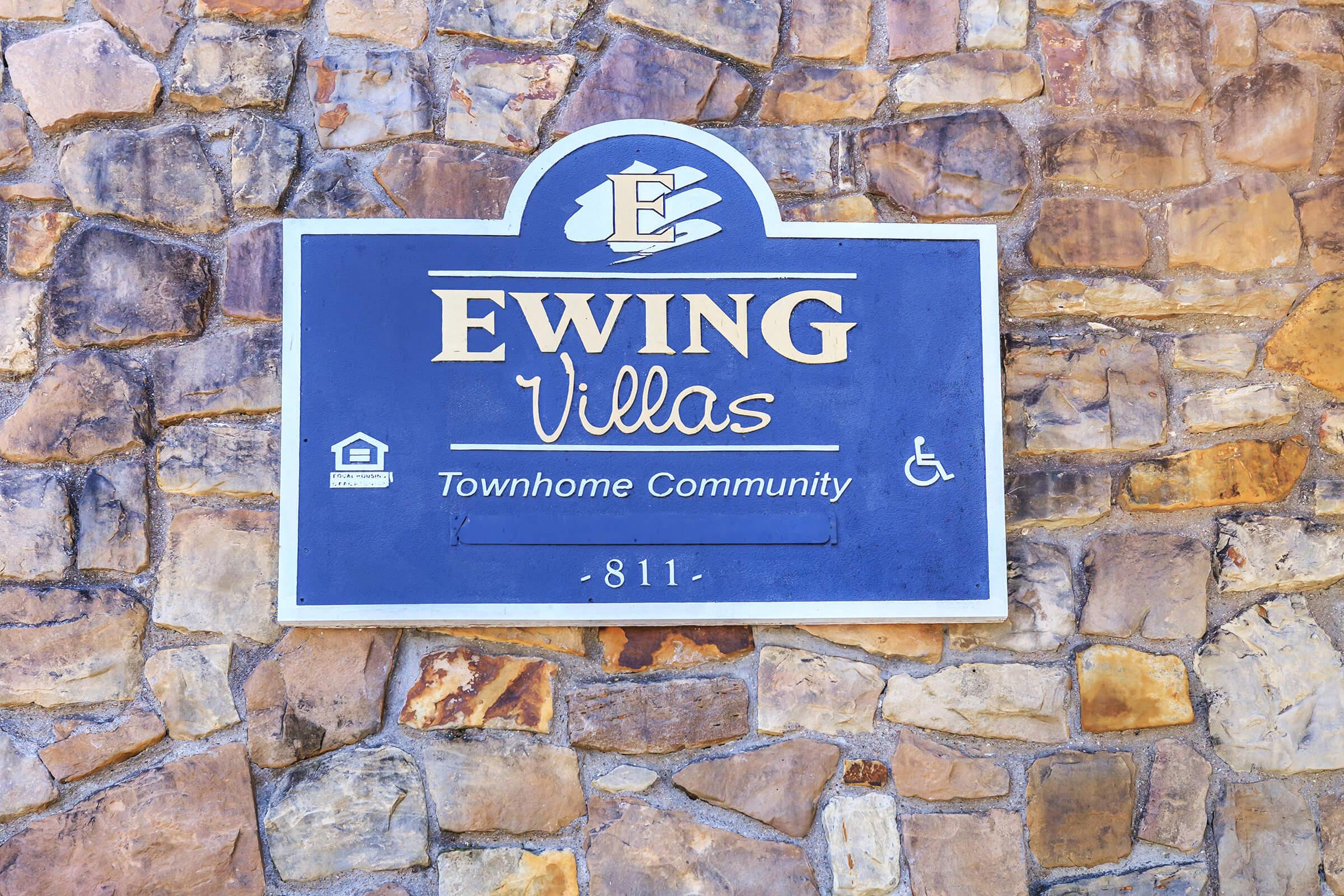 Sign for Ewing Villas, a townhome community, featuring a stone background with the text "Ewing Villas" in decorative font. Includes a logo and symbols for accessibility and amenities. The address "811" is also displayed.