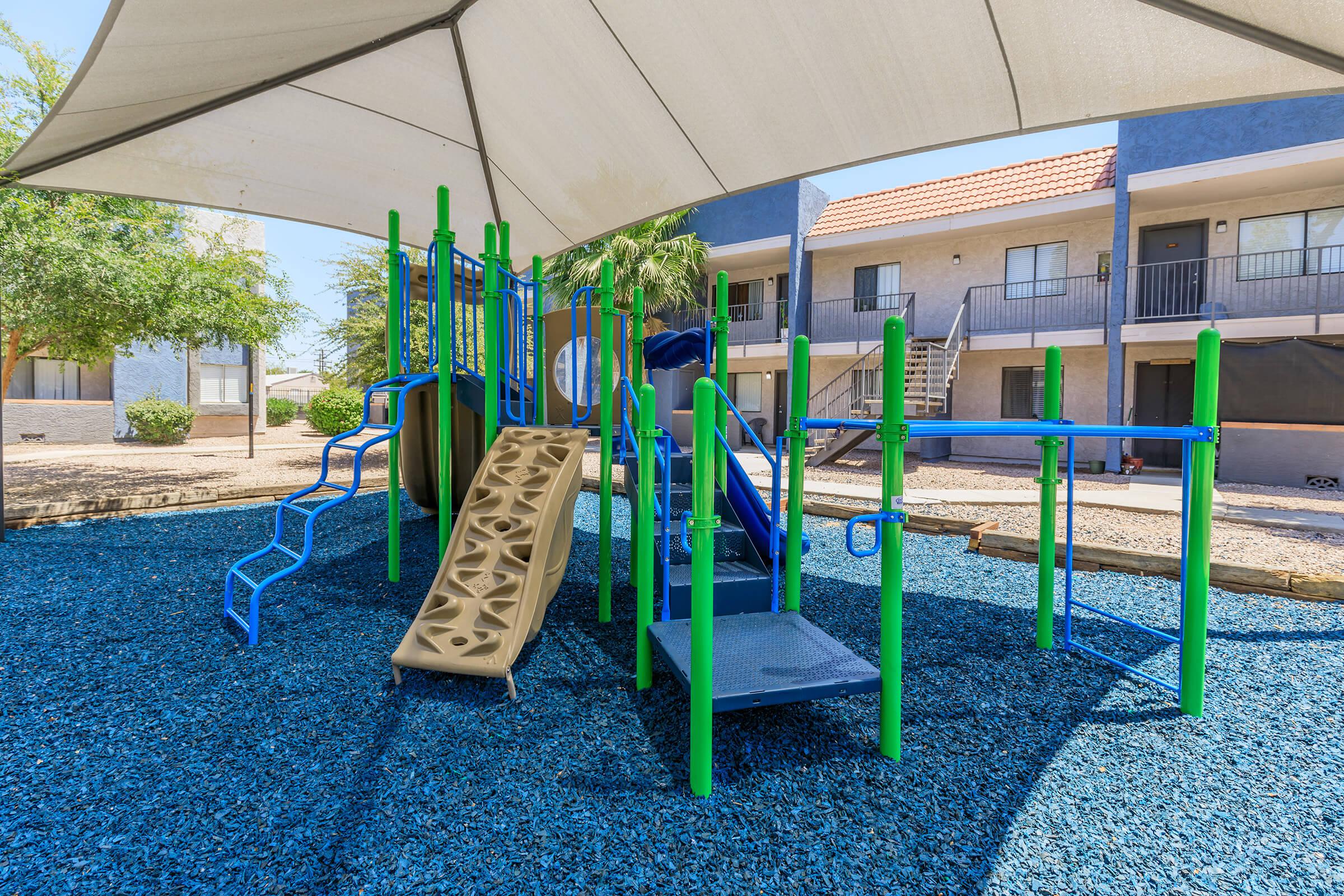 Outdoor green and blue playground set covered by a large shaded awning