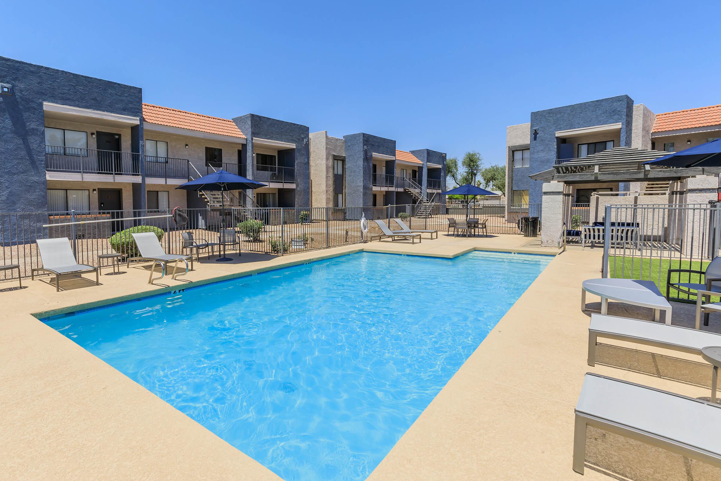 Large blue outdoor swimming pool surrounded by pool chairs and Phoenix apartments for rent