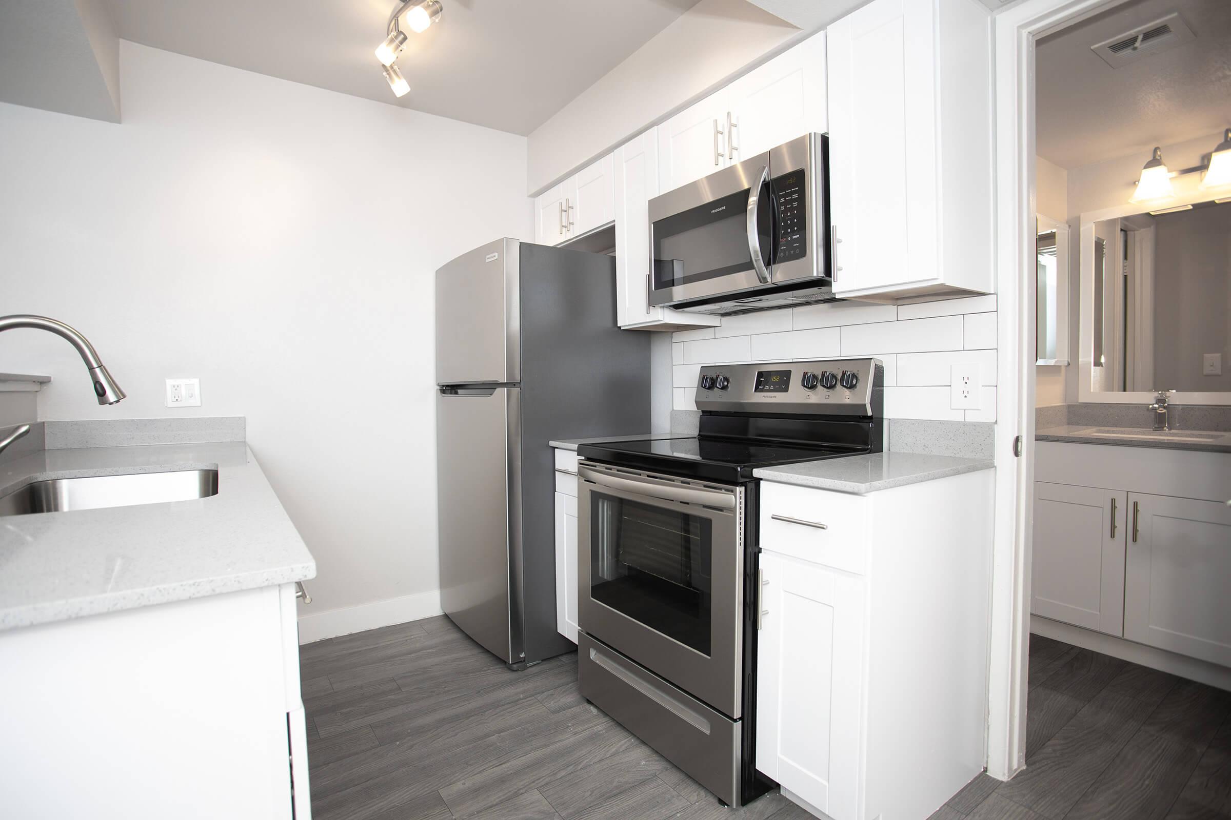 Galley way kitchen with stainless steel appliances, grey quartz counter tops, and white cabinets