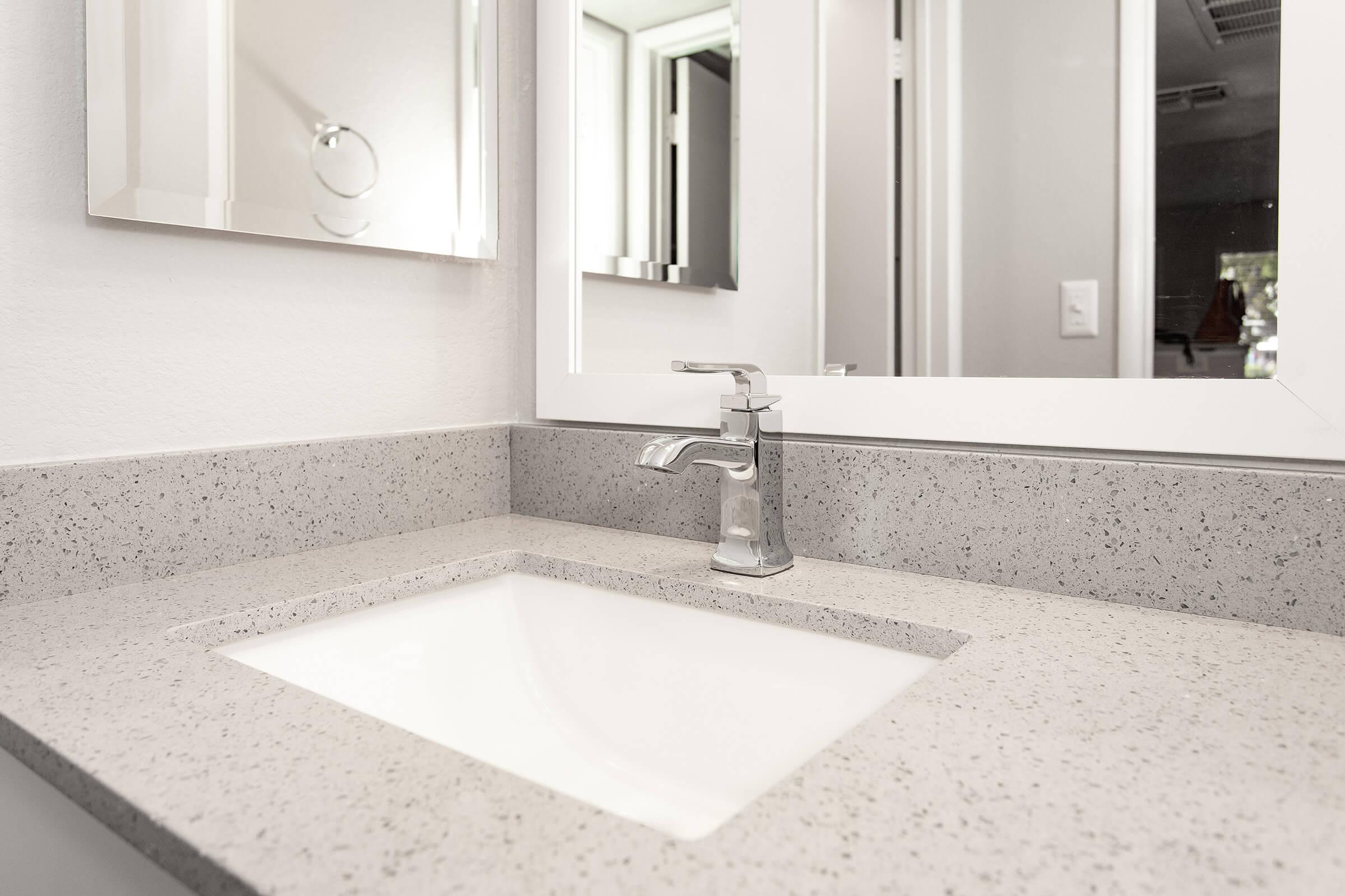 Close up of bathroom sink vanity with silver faucet and grey quartz countertops