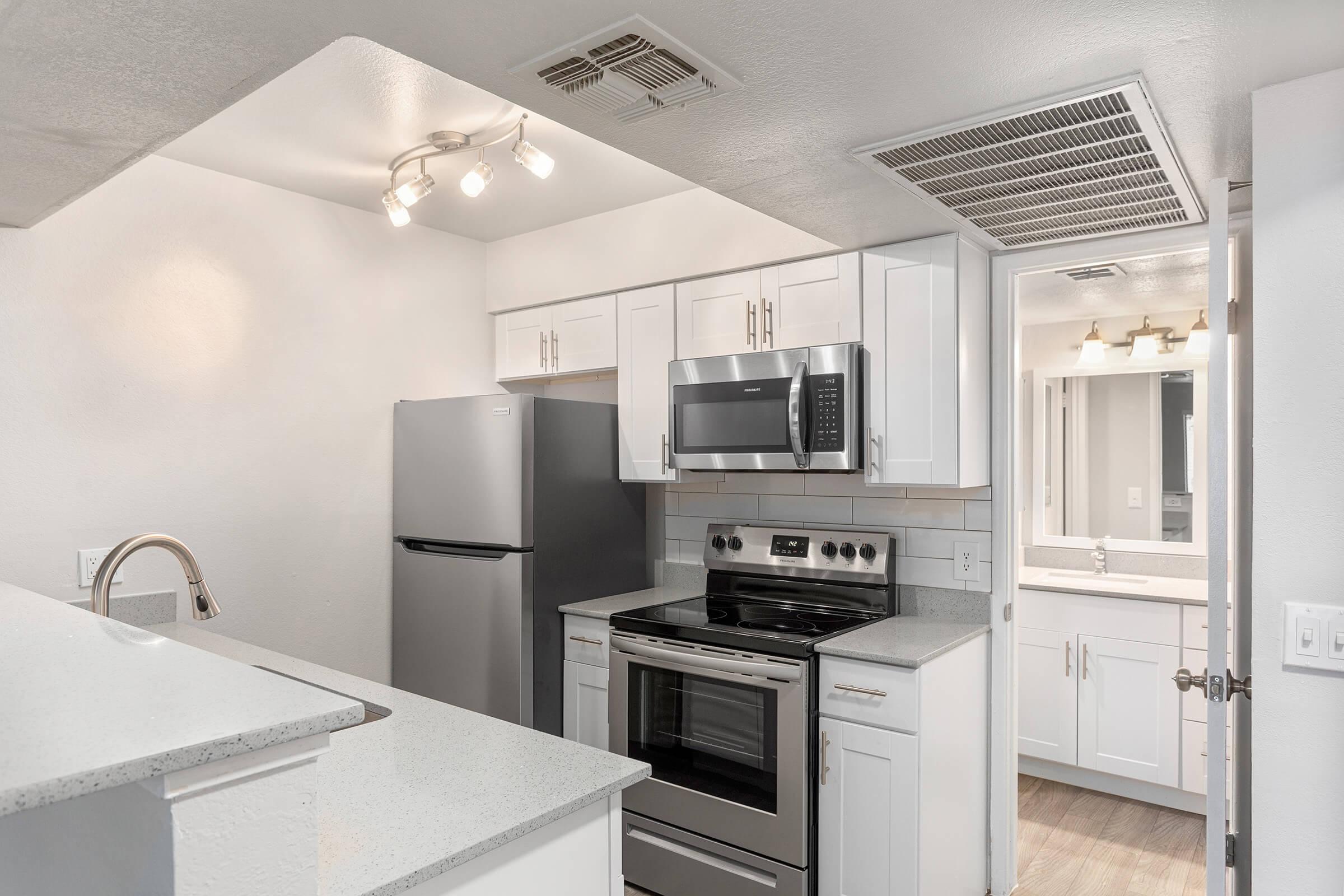 Kitchen with stainless steel appliances, white shaker cabinets, and grey quartz countertops